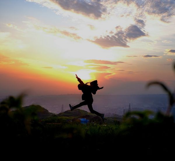 Silhouette of a man stretching at sunrise with a vibrant sky.
